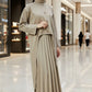 Woman wearing a beige outfit with a pleated skirt on a plain background