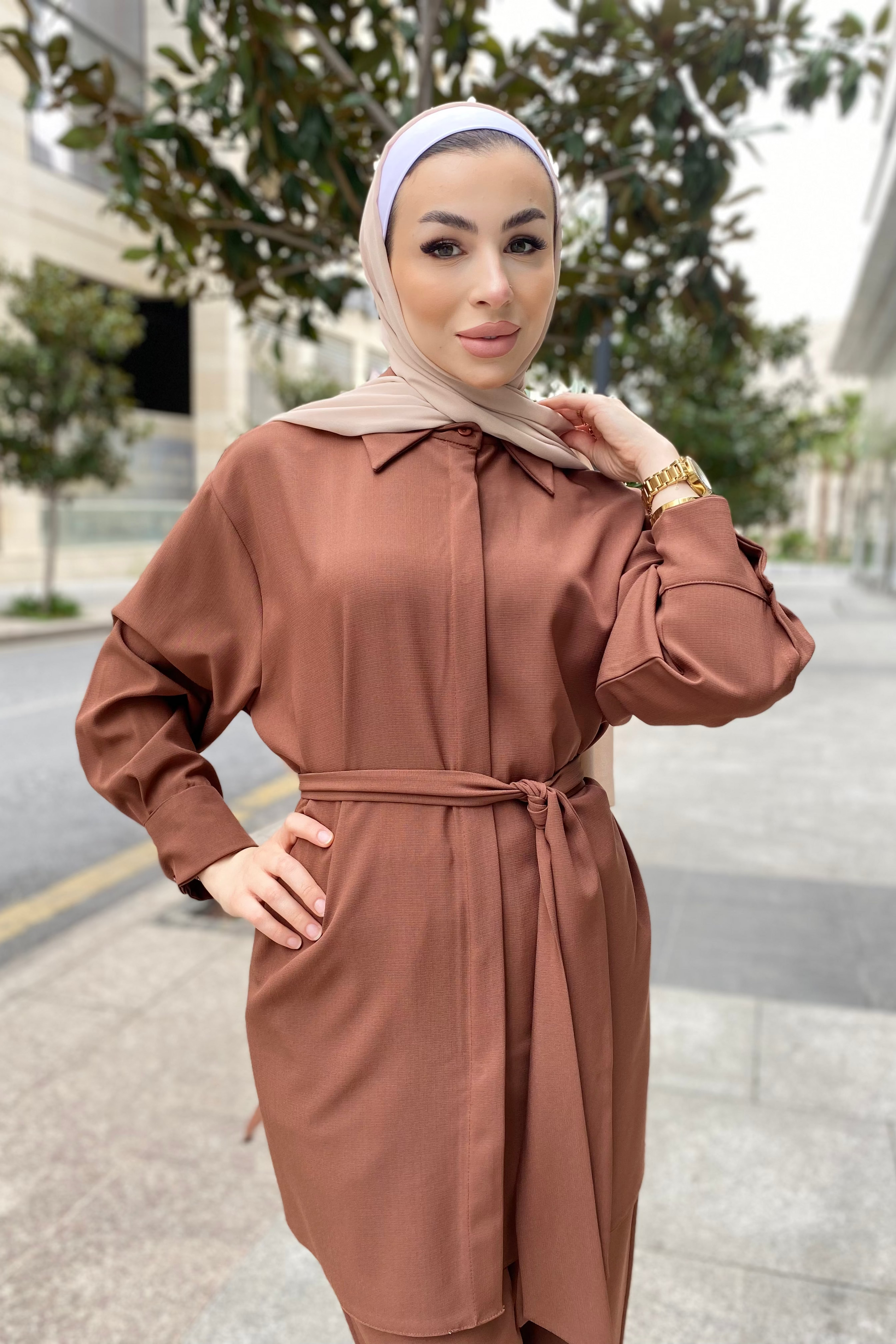 Woman wearing a brown outfit with a headscarf on a street.
