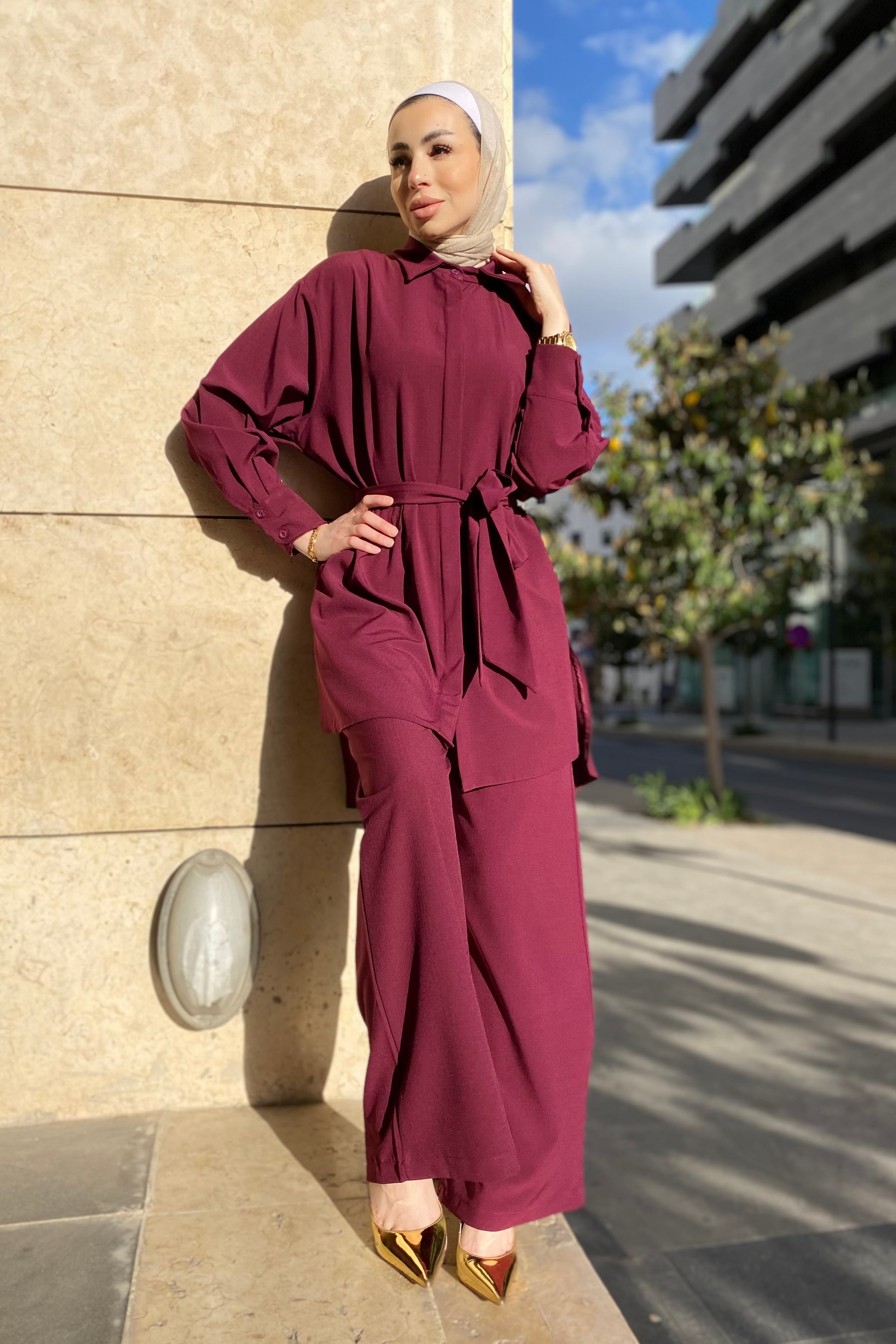 Woman in a burgundy outfit standing against a building with a street scene in the background