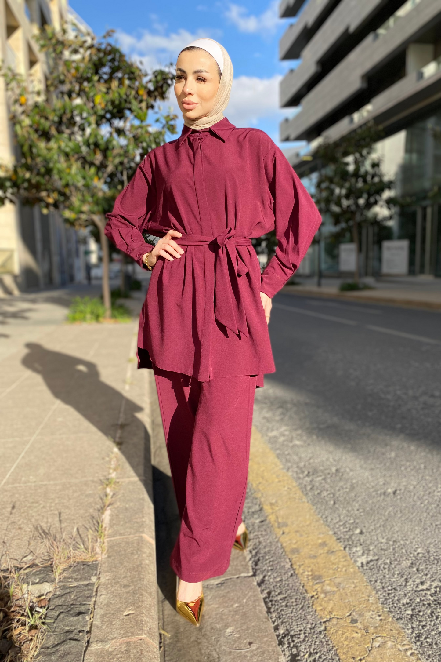 Woman in a maroon outfit standing on a street with buildings and trees in the background