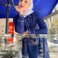 Woman in a blue outfit with a hijab standing under a blue umbrella.