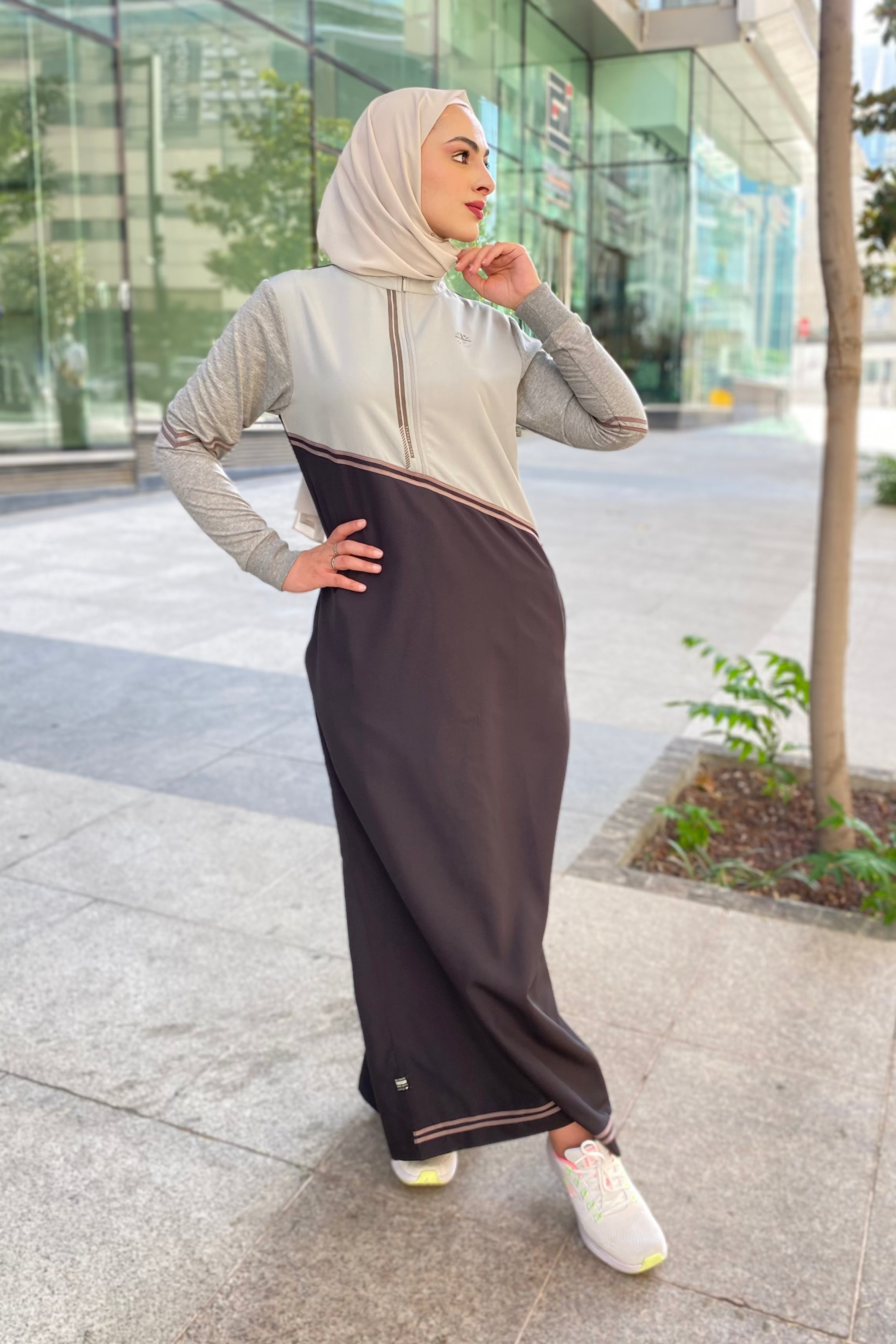 Woman wearing a gray top and brown pants with a hijab in an urban setting.