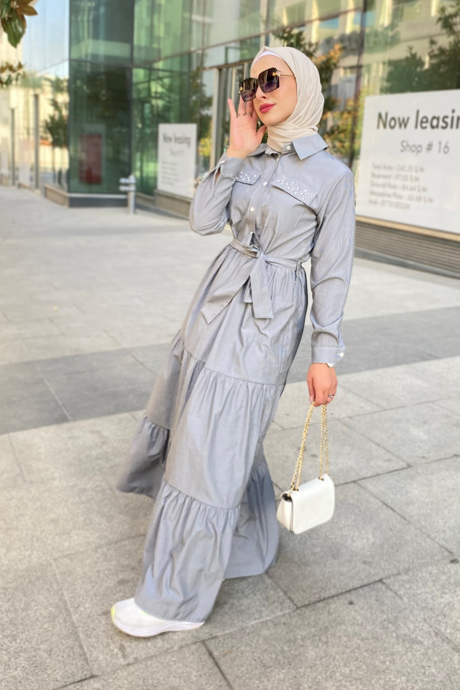 Woman in a gray outfit with a hijab standing on a city street.