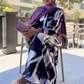 Woman wearing a patterned dress and purple hijab outdoors.
