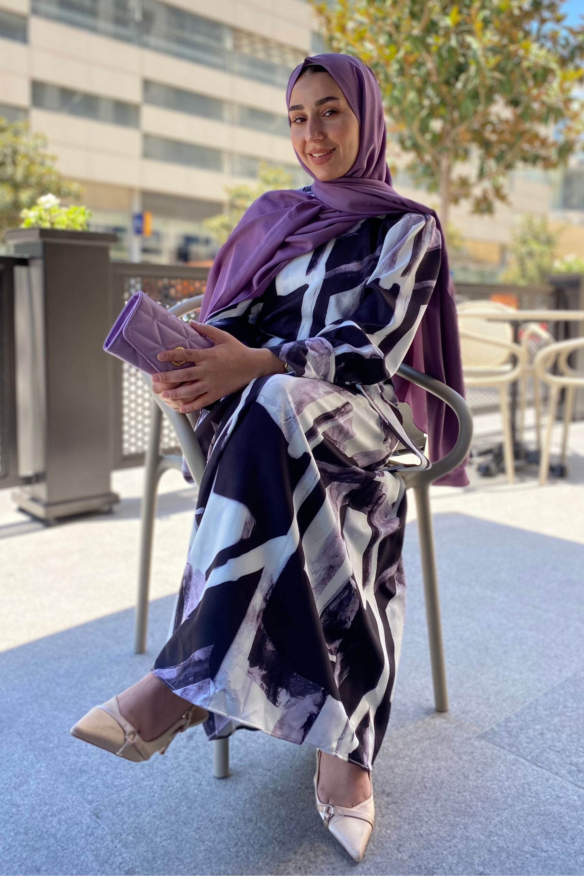 Woman wearing a patterned dress and purple hijab outdoors.