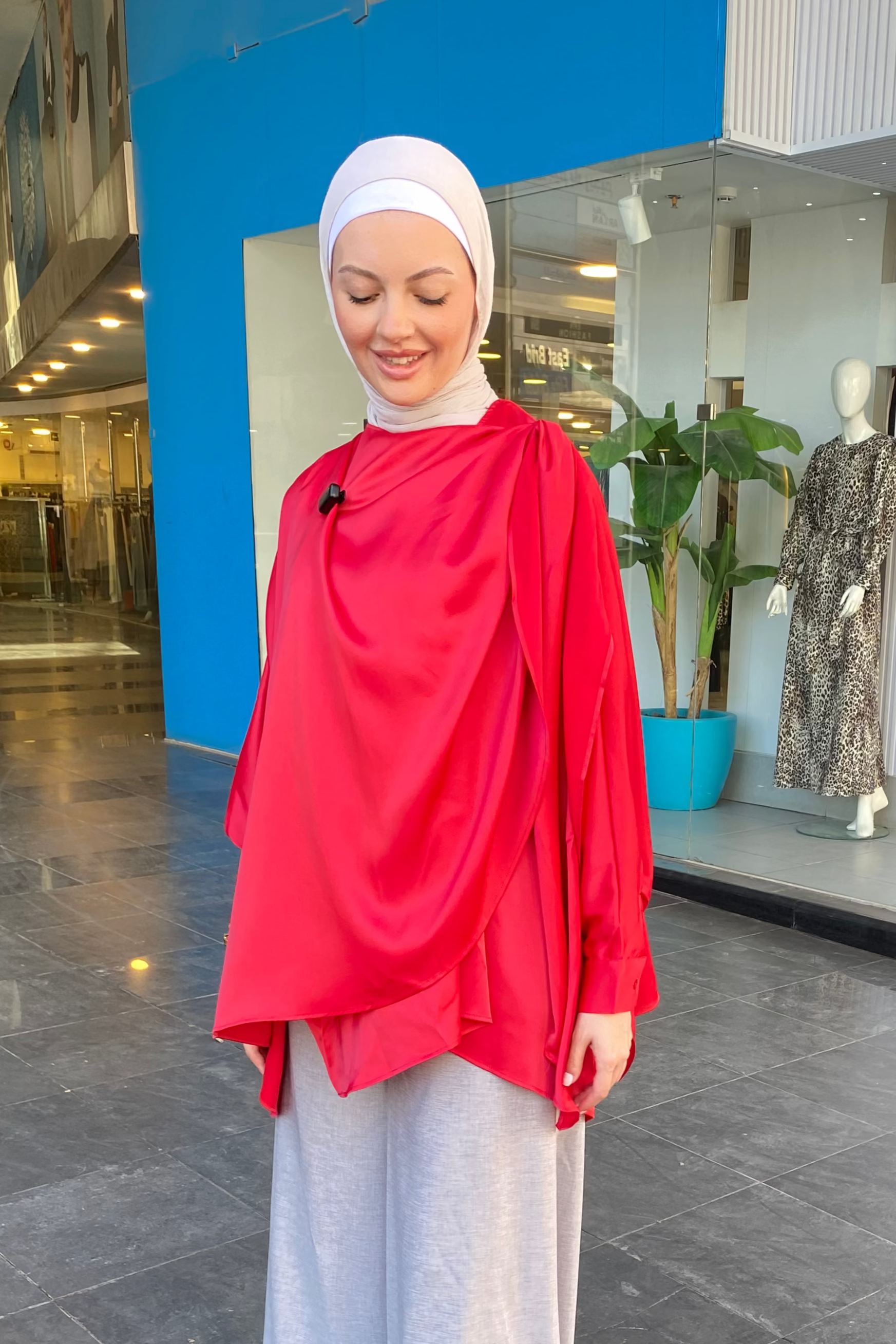 Woman in a red top and white hijab standing in front of a store entrance.