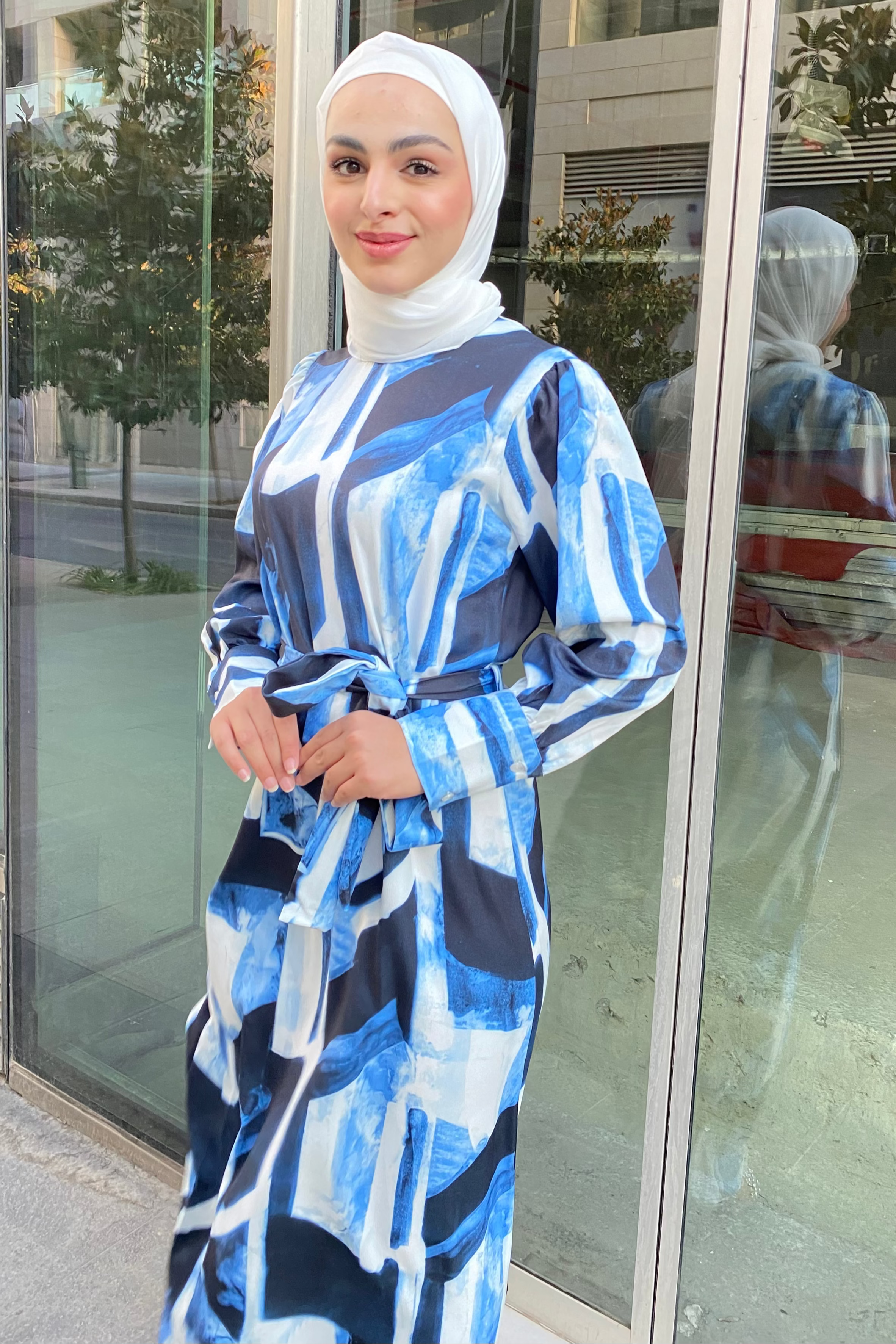 Woman in a blue and white patterned dress standing in front of a glass door.