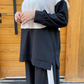 Person wearing a black and white outfit with a hijab in front of a wooden door.