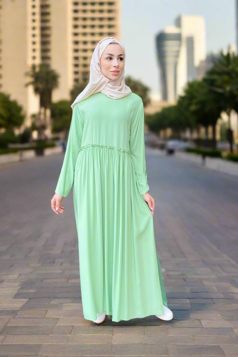 Woman in a light green dress standing in an indoor setting with modern architecture.