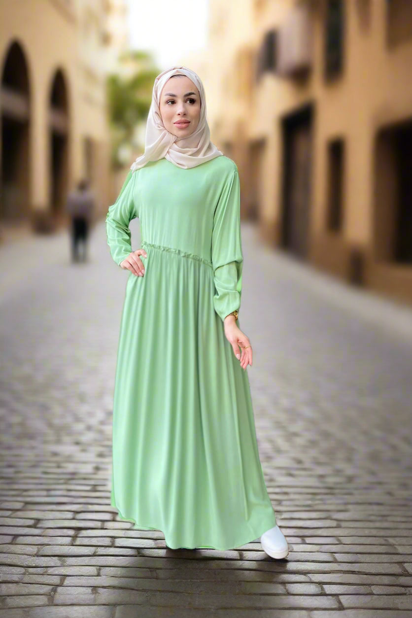 Woman in a light green dress standing in an indoor setting with reflective flooring.