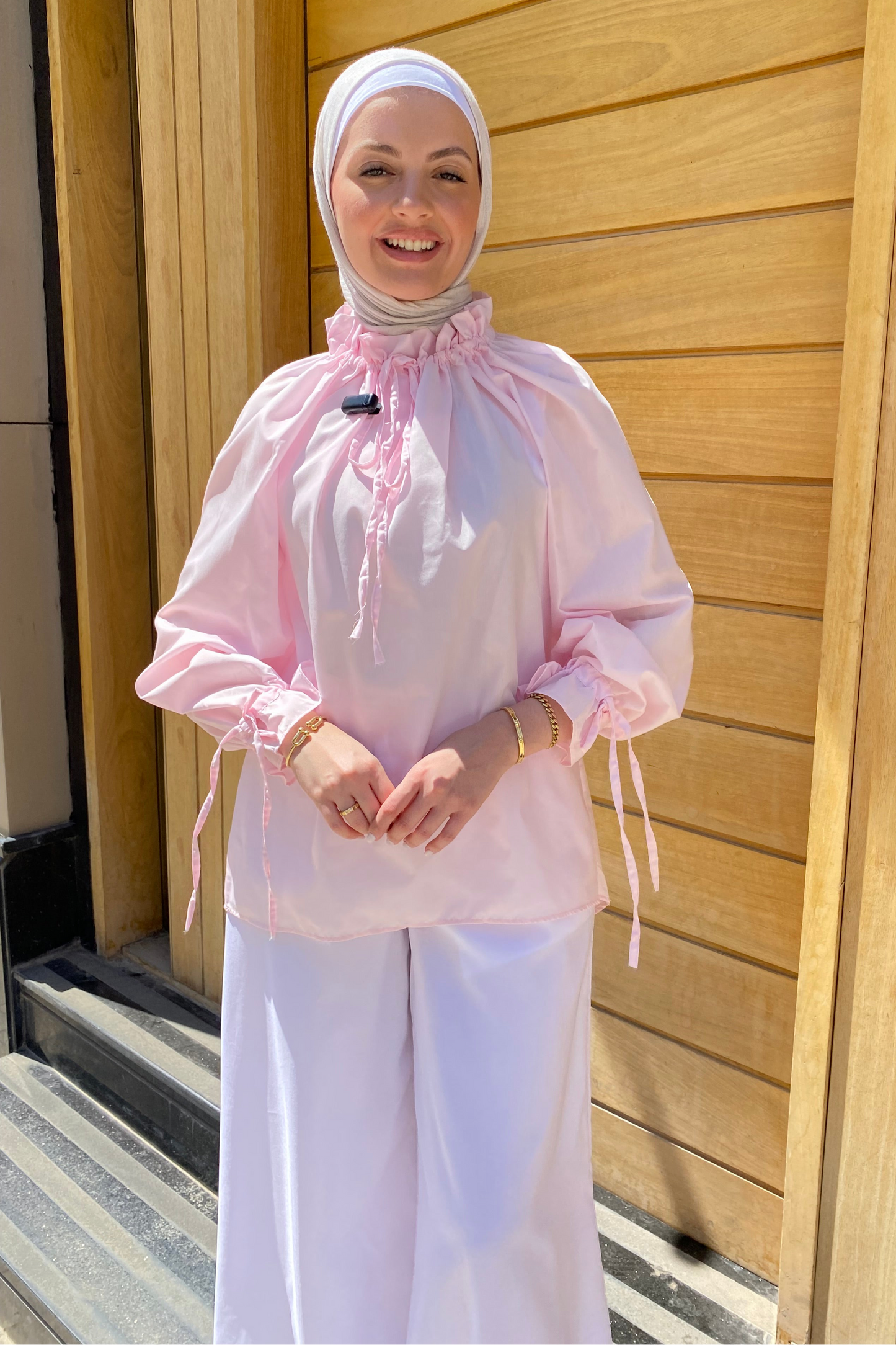 Person wearing a pink outfit with a hijab standing in front of a wooden door.
