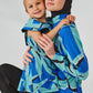Two people wearing blue and green patterned ponchos against a white background