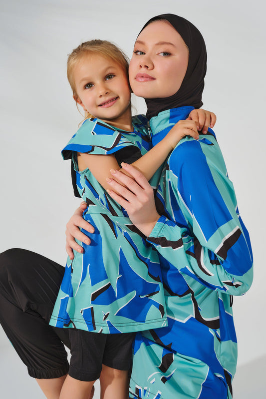 Two people wearing blue and green patterned ponchos against a white background