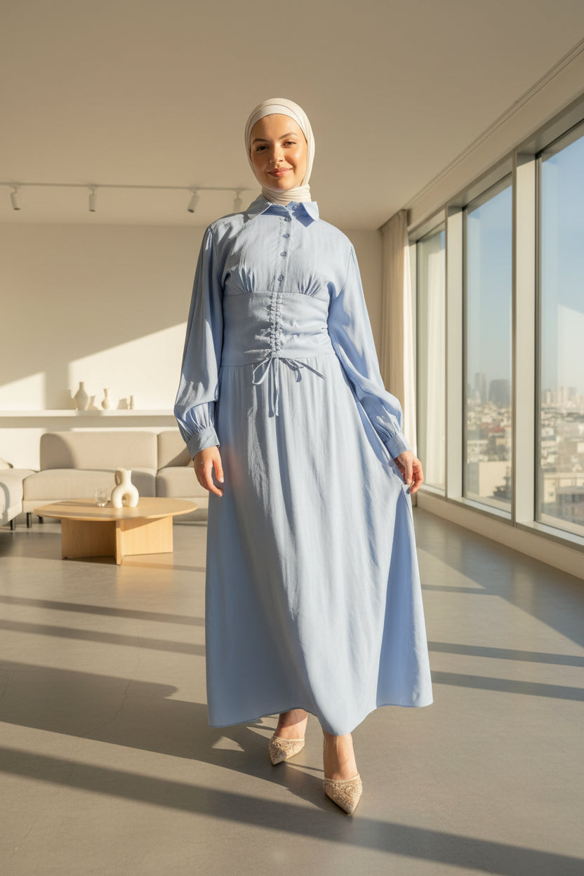 Woman in a light blue dress standing in a modern indoor setting with glass walls.