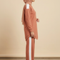 A woman in profile wearing a dusty rose hijab, matching long-sleeve top with white shoulder panels, and matching wide-leg pants with white side stripes, standing against a plain beige studio backdrop.