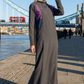Woman in a long, dark gray dress with purple accents standing in front of Tower Bridge.