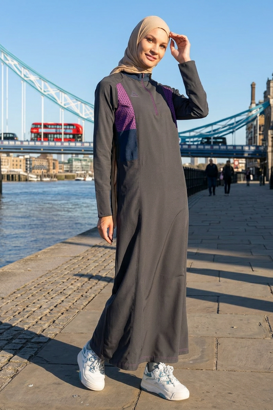 Woman in a long, dark gray dress with purple accents standing in front of Tower Bridge.