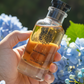 Hand holding a small bottle of Kiehl's product with blue flowers in the background