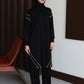 Woman in a black outfit standing in a minimalistic room with a brown bench and white wall.