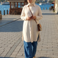 A woman wearing a cream-colored long-sleeve tunic and blue wide-leg jeans walks along a stone pathway with a scenic waterfront view of Istanbul in the background.