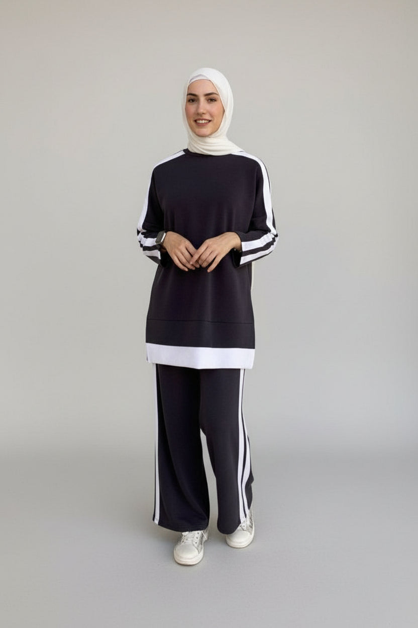 Person wearing a black and white outfit with a hijab standing in front of a door.