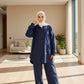 Person wearing a navy blue outfit with a white hijab standing in front of a wooden door.
