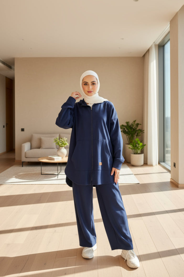 Person wearing a navy blue outfit with a white hijab standing in front of a wooden door.