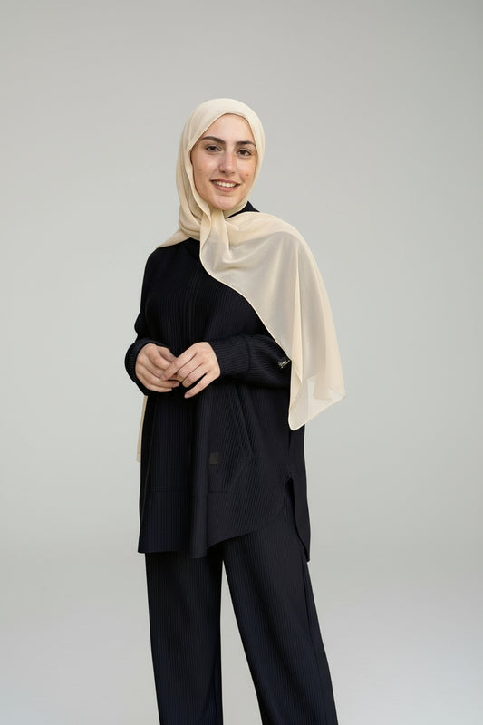 Woman wearing a black outfit with a beige hijab standing in front of a light blue door.