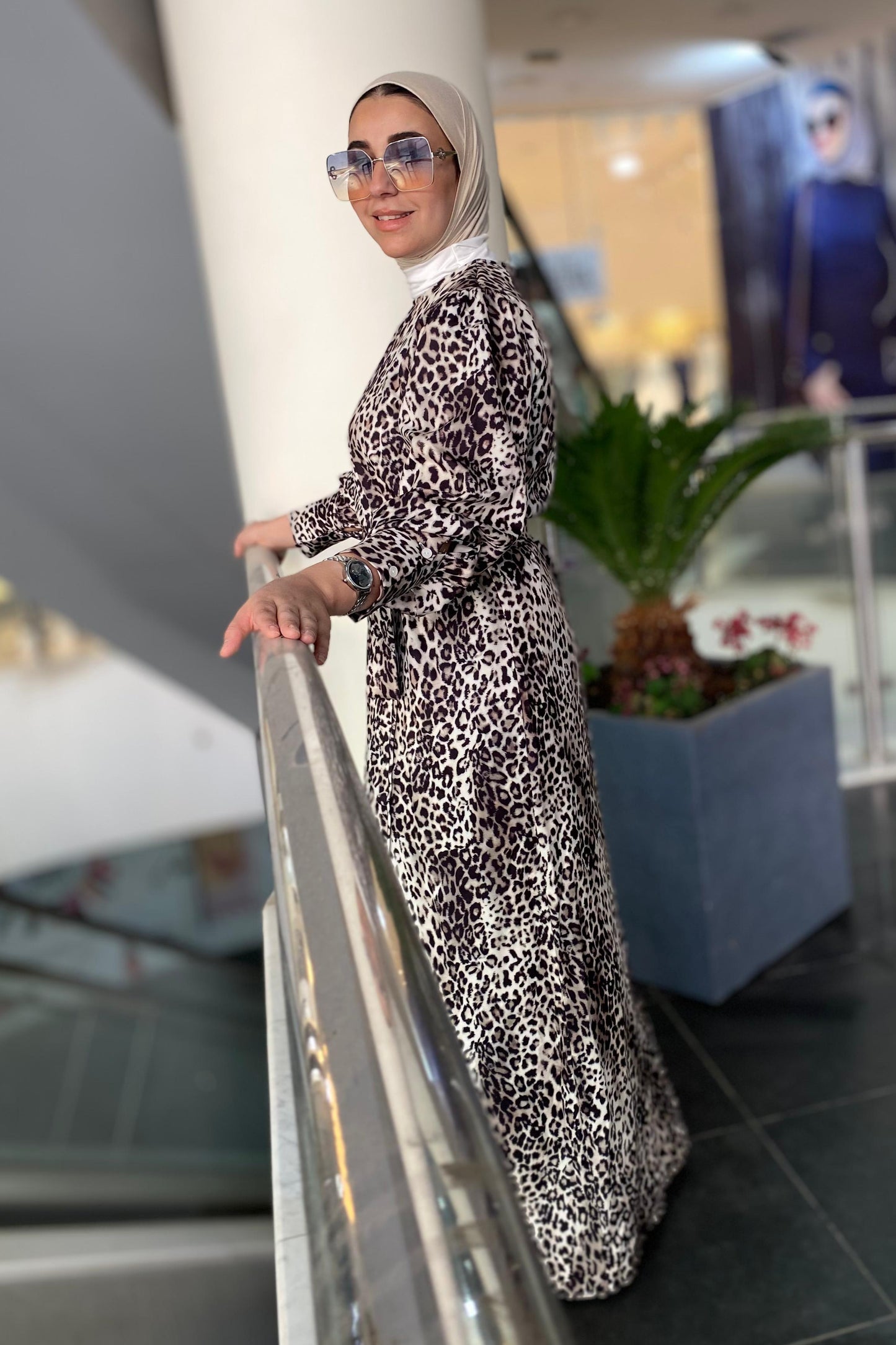 Woman in a patterned dress standing in a modern indoor setting with a plant and architectural elements.