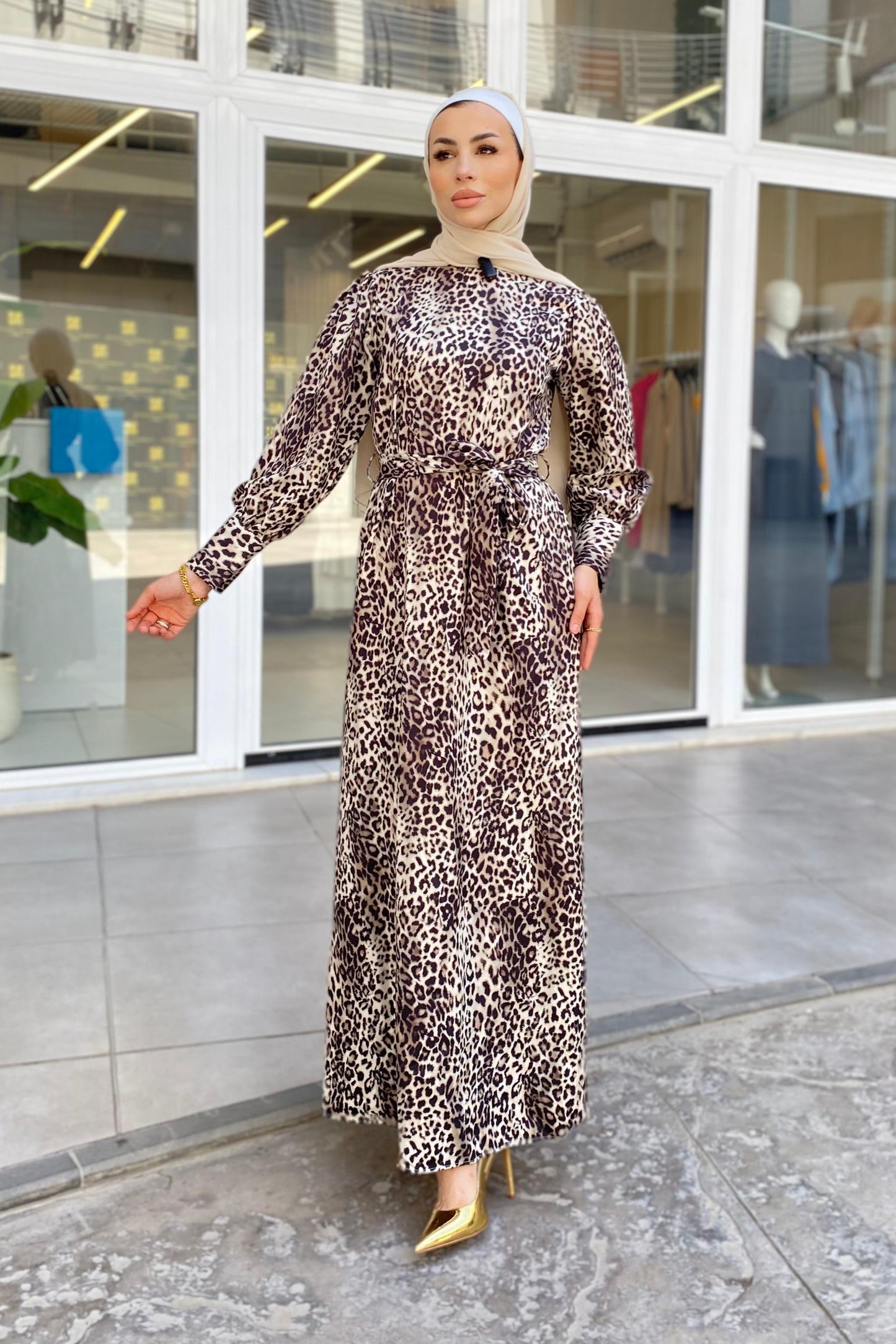 Woman in a leopard print dress standing outside a building with large windows.