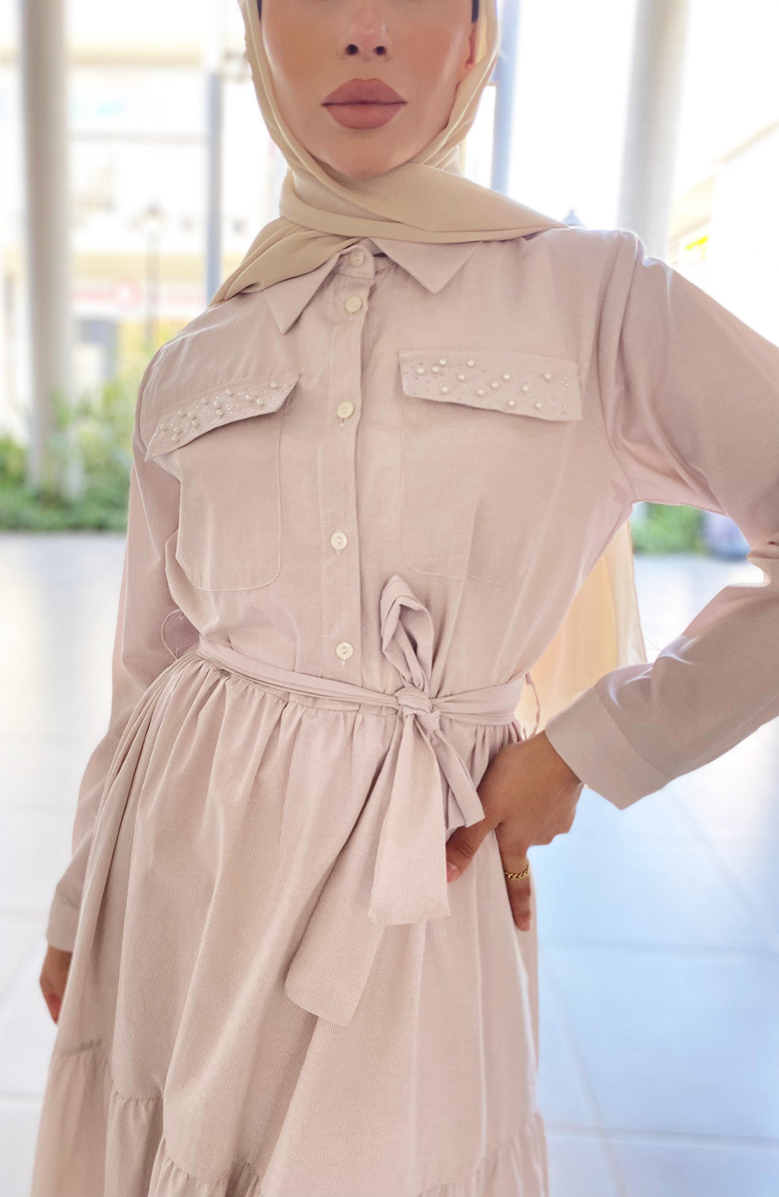 Woman wearing a beige dress with a hijab in an outdoor setting