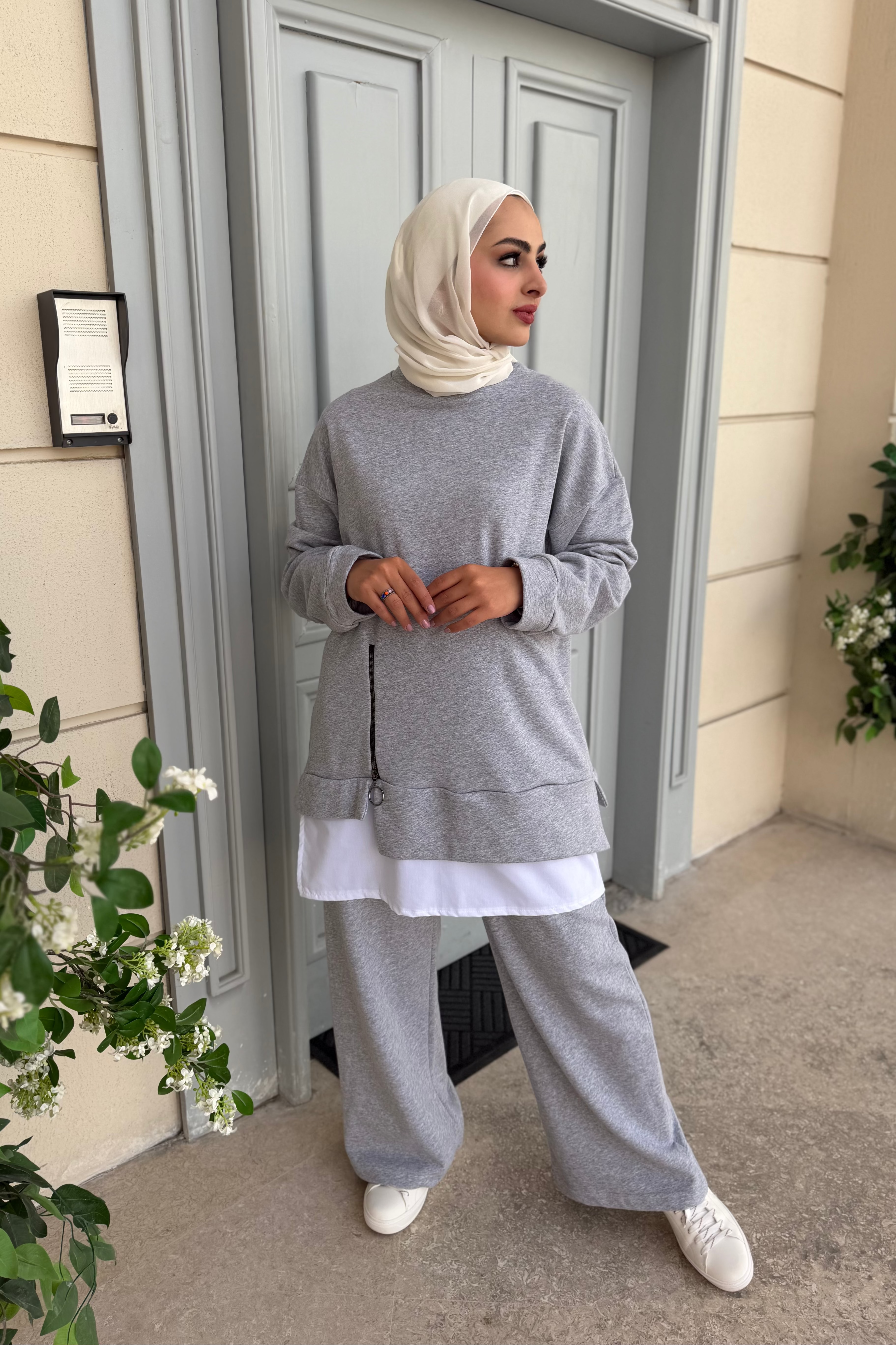 Woman in gray outfit standing outside a building with plants around