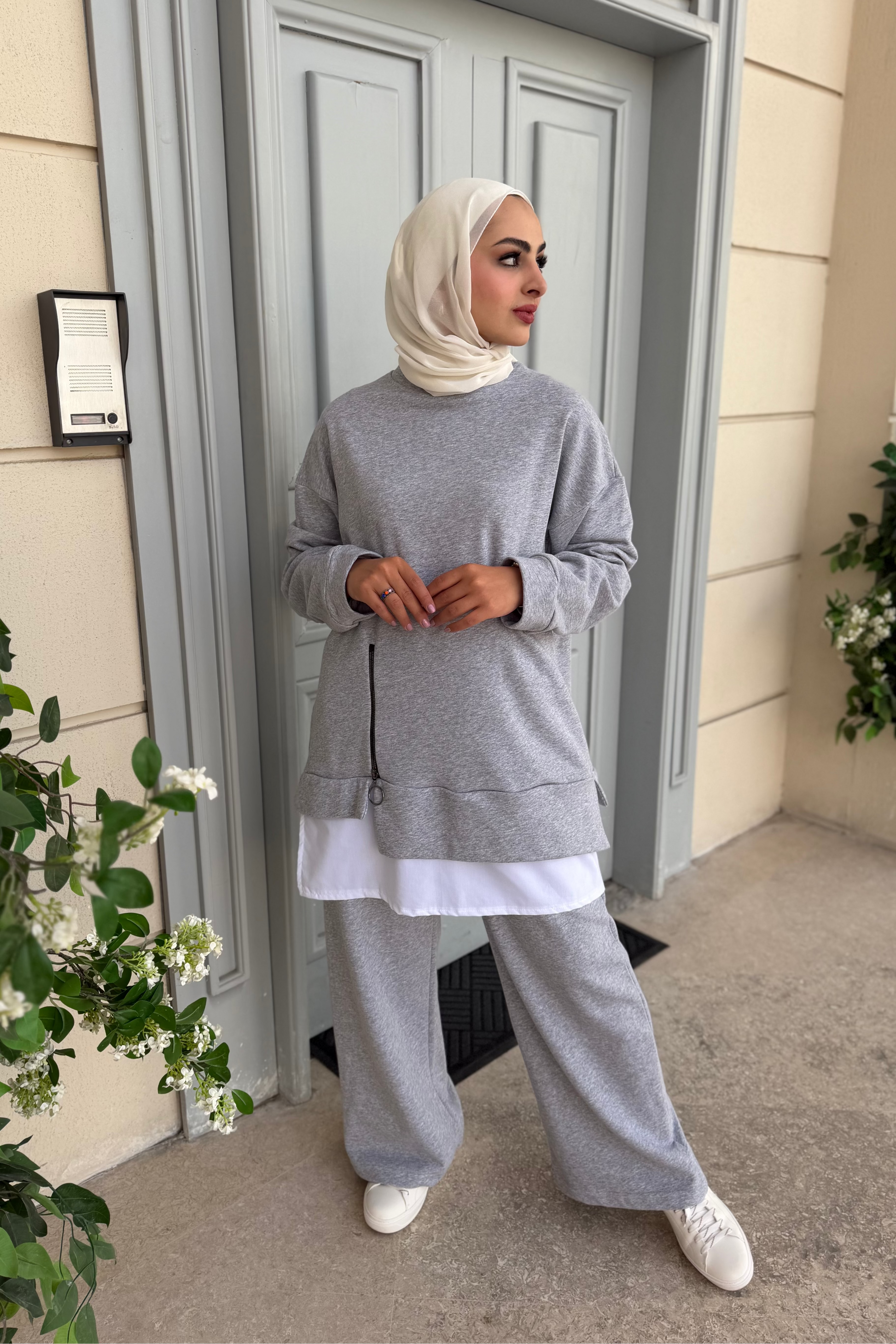 Woman in gray outfit standing outside a building with plants around