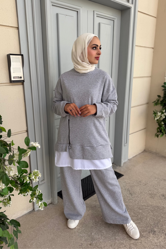 Woman in gray outfit standing outside a building with plants around